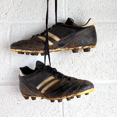 A pair of muddy black football boots hang in a white-walled changing room.